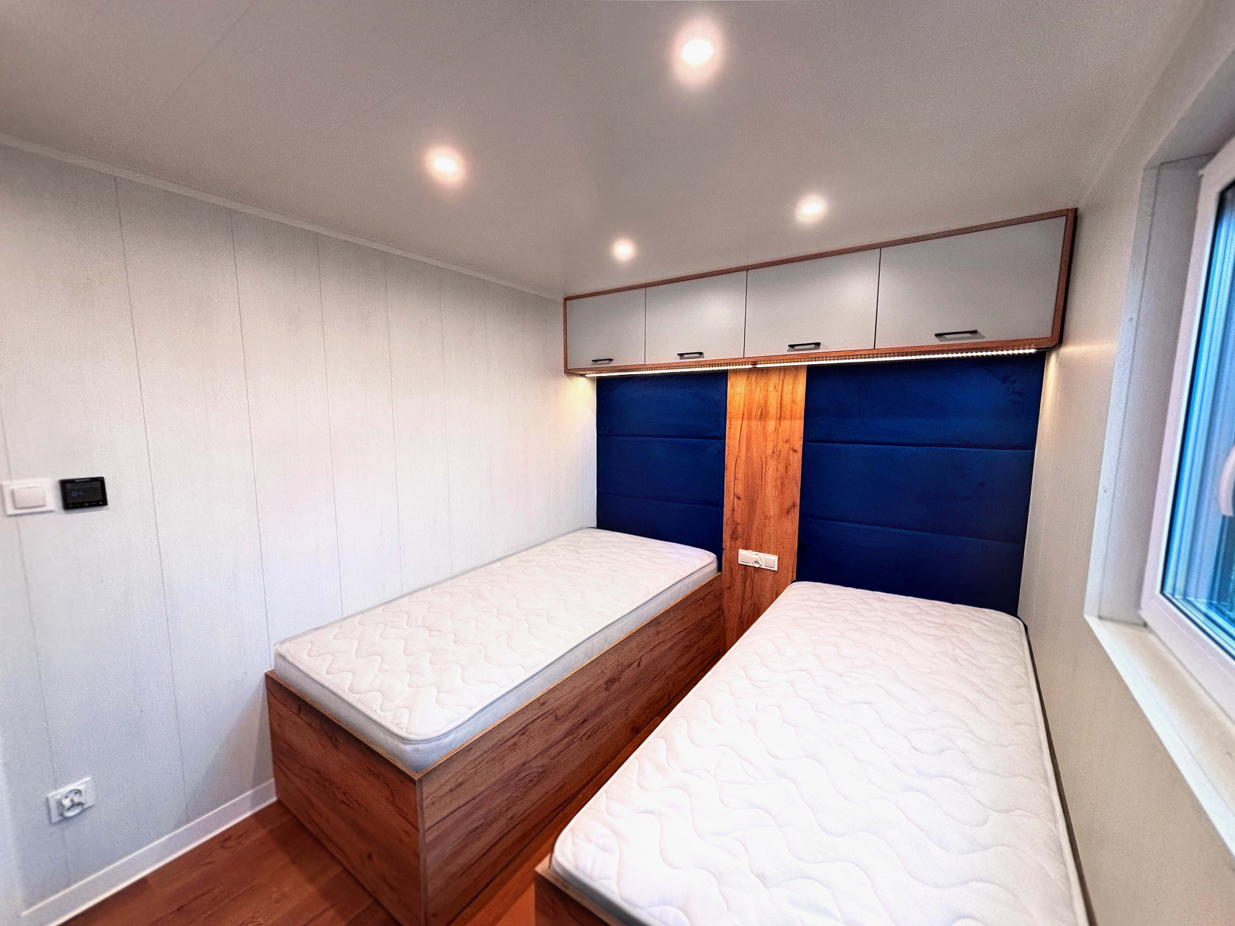 Sypialnia w domku mobilnym z dwoma łóżkami i zabudową nad nimi